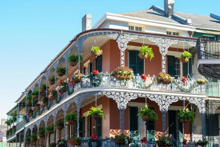 Historic building with ornate iron balconies, plants, and blue shutters under a clear blue sky.