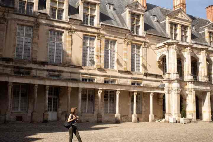 Person standing in a cobblestone courtyard with a historic building in the background.