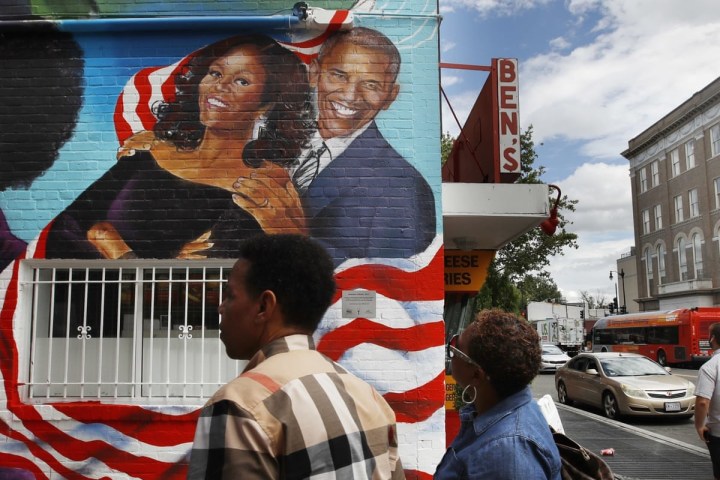 Mural on building wall with red, white stripes, people walking by on sidewalk.
