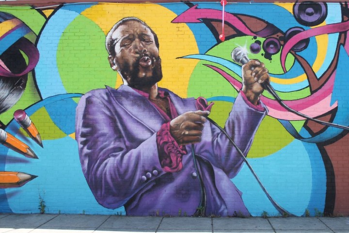 Colorful mural of a man singing passionately into a microphone on a brick wall.