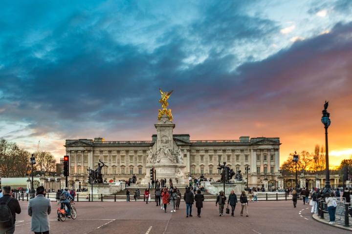 People walking near a statue in front of a large building at sunset.