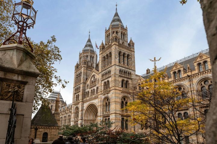 Historic building with towers, arched windows, and autumn trees under a blue sky.