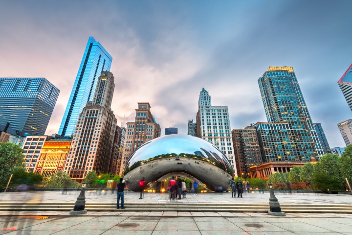 City skyline with reflective sculpture and scattered people in foreground, under a cloudy sky.