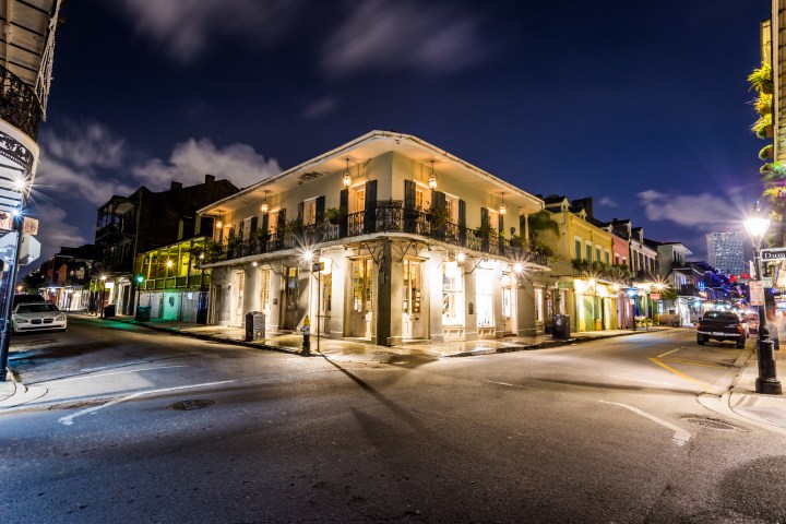 Illuminated French Quarter street corner at night with historic buildings and parked cars.