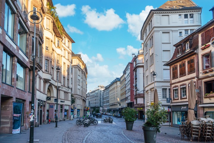 Cobblestone street lined with historic buildings under a blue sky with scattered clouds.