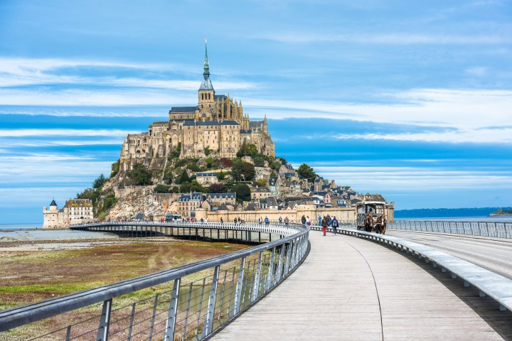 Mont Saint-Michel with causeway and people under a blue sky.