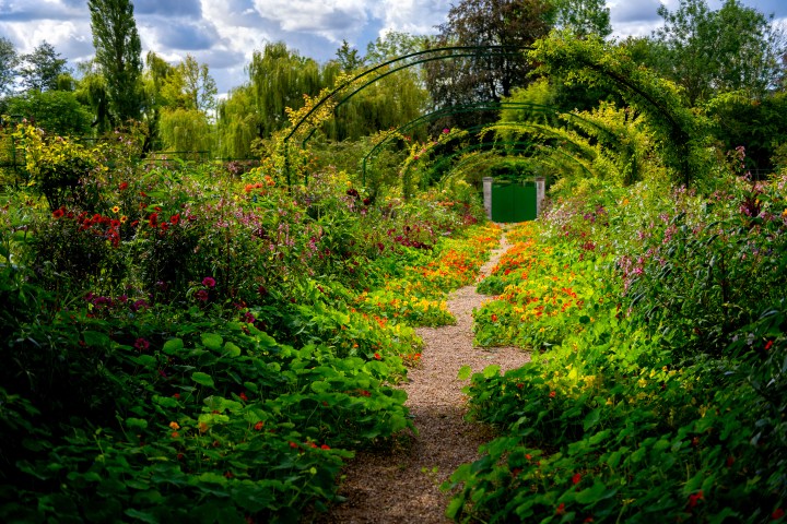 A vibrant garden path with colorful flowers and archways under a cloudy sky.