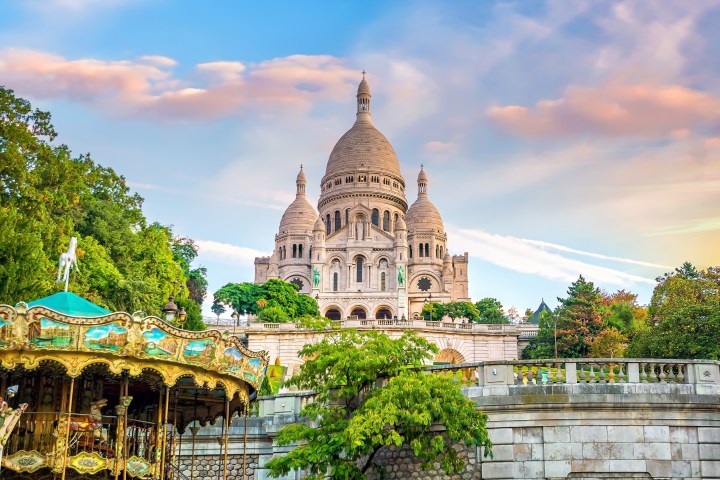 Sacré-Cœur Basilica in Paris with a carousel and trees in the foreground during sunset.