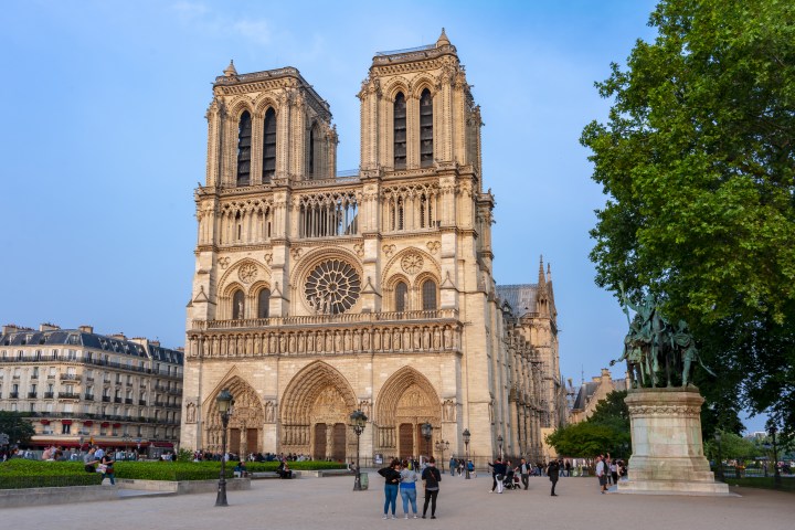 Front view of Notre Dame Cathedral with people and trees around.