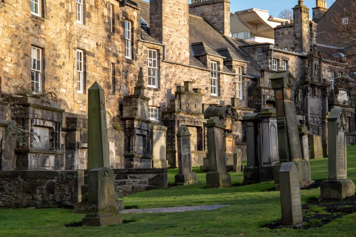 Historic stone buildings and gravestones in a sunlit cemetery.