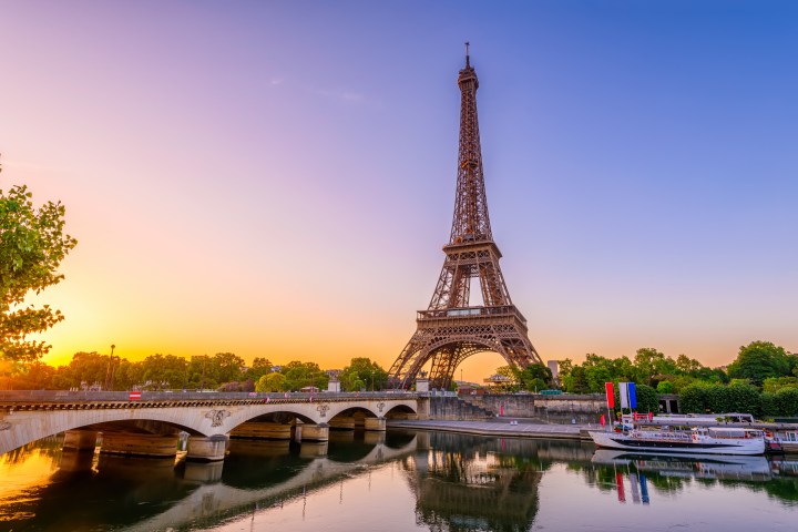 Eiffel Tower at sunset with a bridge and boats on the river.