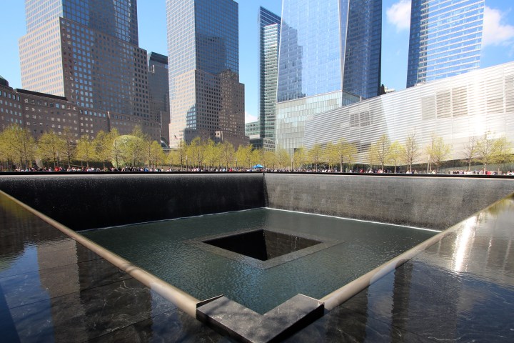 Memorial pool with cascading water surrounded by trees and skyscrapers.