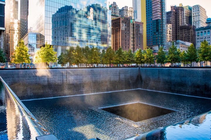 Reflecting pool at memorial site with city buildings and trees in the background.