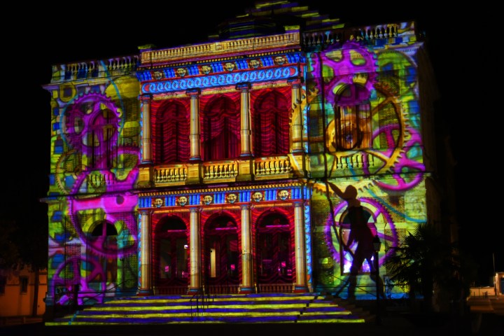 Ornate building with colorful gear projections at night.
