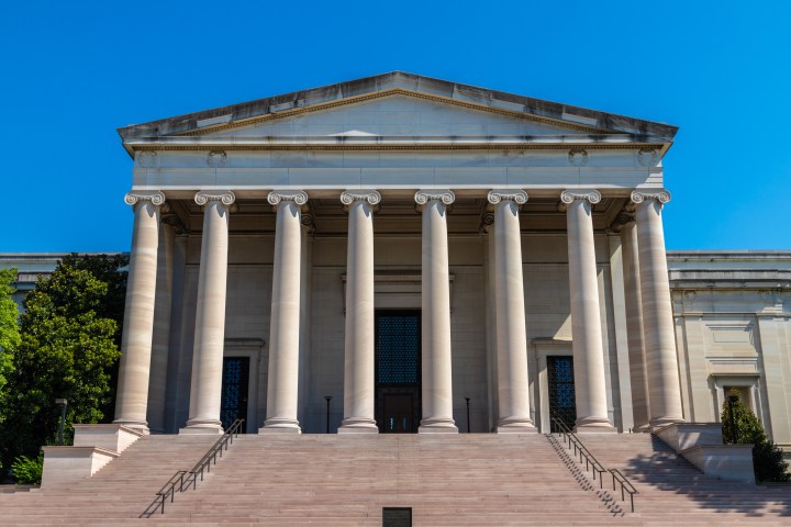 Classical building with six columns and steps, under a clear blue sky.
