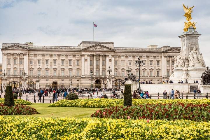 Buckingham Palace with gardens and people in the foreground on a cloudy day.
