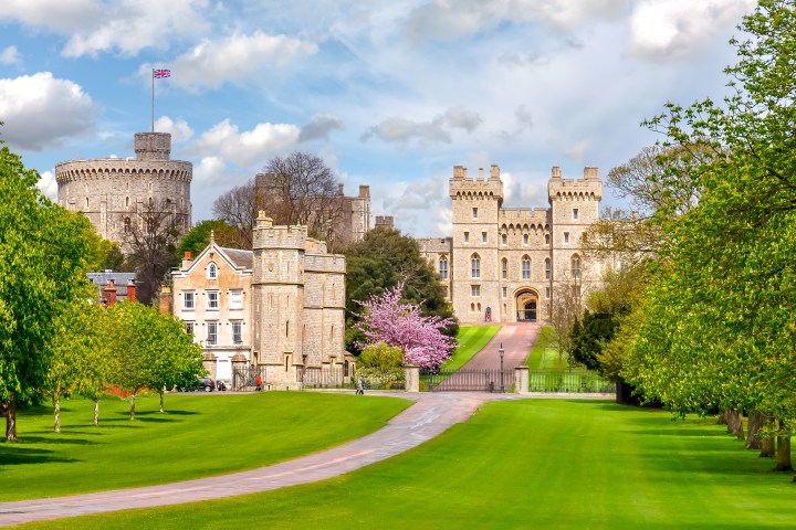 Windsor Castle with green lawns and trees under a cloudy sky.