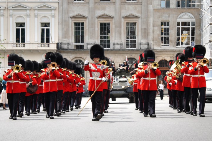 Marching band in red uniforms and bearskin hats performs on a city street.