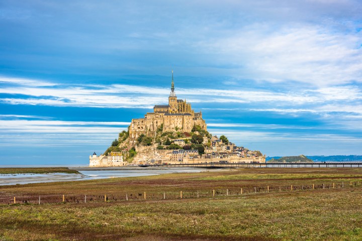 Mont Saint-Michel abbey on rocky island with cloudy sky background.