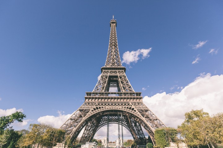 Eiffel Tower framed by trees under a clear blue sky with clouds.