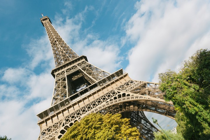 Eiffel Tower viewed from below with a clear sky and surrounding trees.