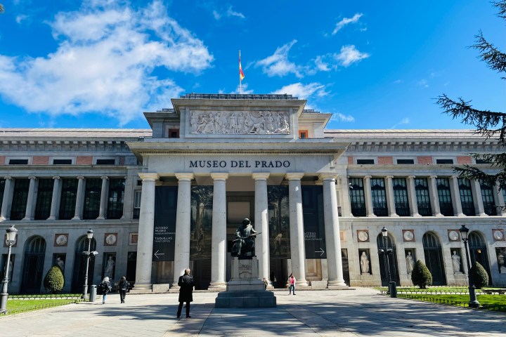 Front view of Museo del Prado entrance with clear blue sky and a few people walking.