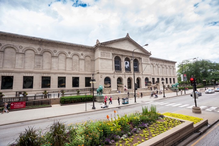 Historical museum building with columns and steps, surrounded by pedestrians and traffic.