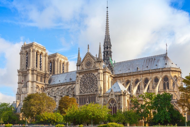Notre Dame Cathedral with blue sky and trees in the foreground.