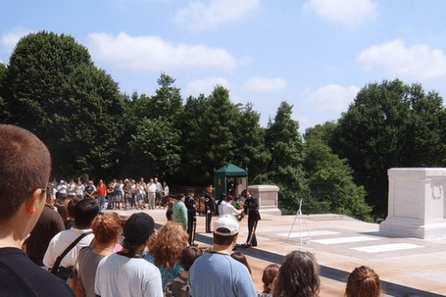 Ceremony with guards and crowd at a monument surrounded by trees.