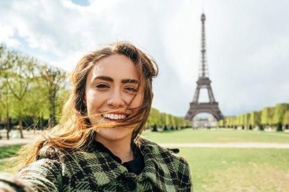Woman taking selfie with Eiffel Tower in background on a sunny day.