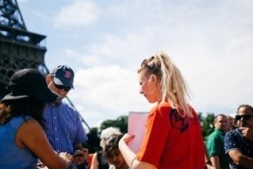 Group of people near Eiffel Tower under a clear sky, one person holding a red folder.