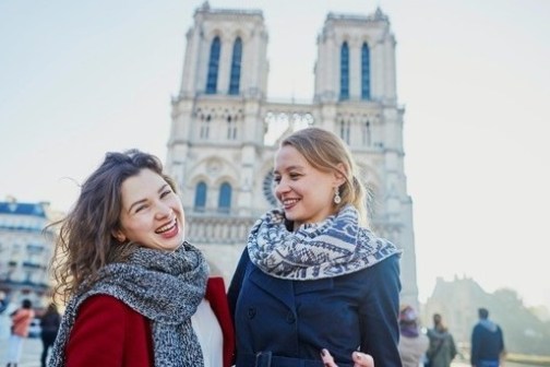 Two women smiling in front of Notre-Dame Cathedral on a sunny day.