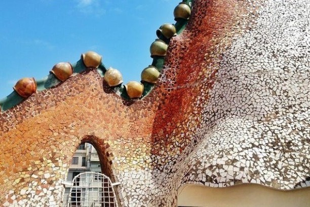 Close-up of a mosaic rooftop with organic shapes and colorful tiles under a blue sky.
