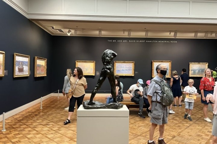 Museum gallery with a bronze sculpture and people viewing framed paintings on the walls.