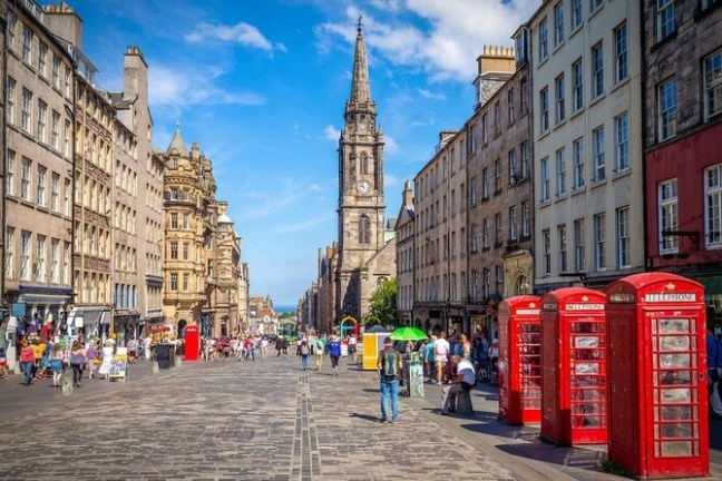 A bustling city street with red phone booths and a tall clock tower under a blue sky.