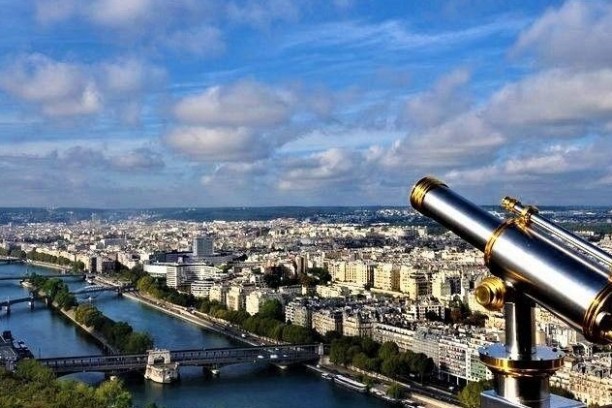 Telescope on Eiffel Tower overlooks Paris cityscape and Seine River under blue sky with clouds.