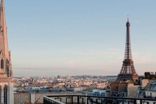 Skyline of Paris with the Eiffel Tower and a church spire, viewed from a rooftop at sunset.