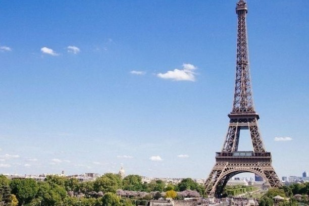 Eiffel Tower with blue sky and scattered clouds above green trees in Paris.