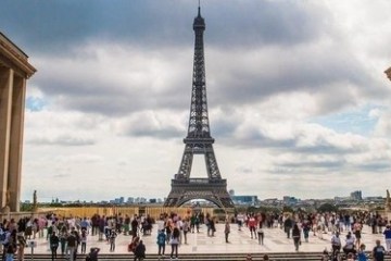 Crowd gathered near Eiffel Tower under cloudy sky in Paris.
