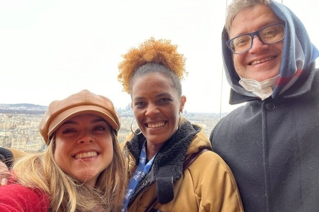 Three people smiling on a city overlook, wearing coats and hats.