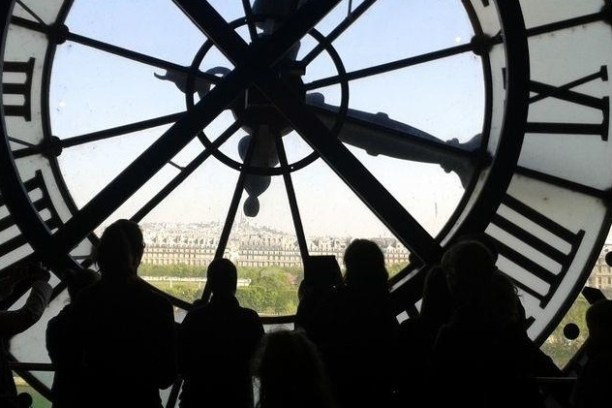 Silhouettes of people in front of a large clock face with city view through it.