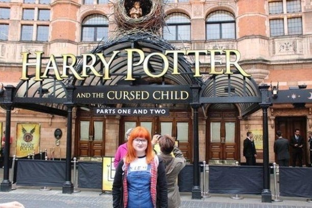 Person with orange hair stands in front of Harry Potter theater entrance.