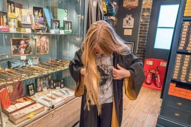 Child wearing a wizard robe in a themed shop with wand displays.