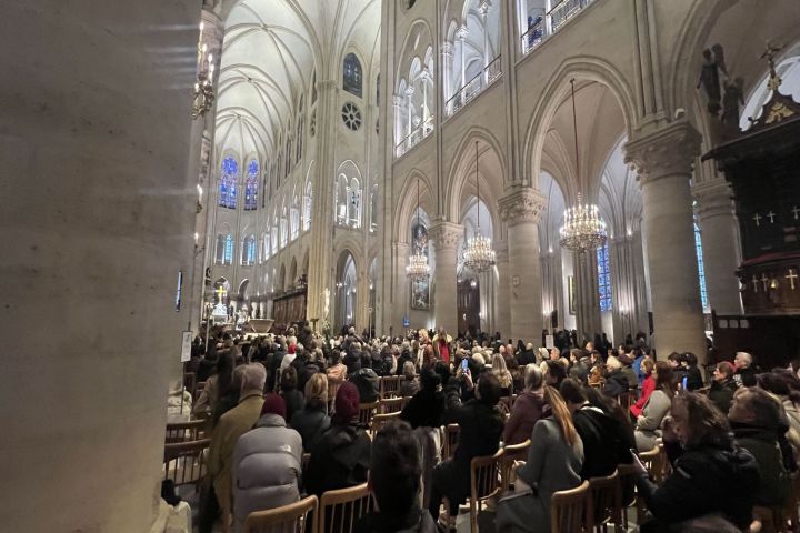 Large crowd seated inside a grand cathedral with arched ceilings and chandeliers.