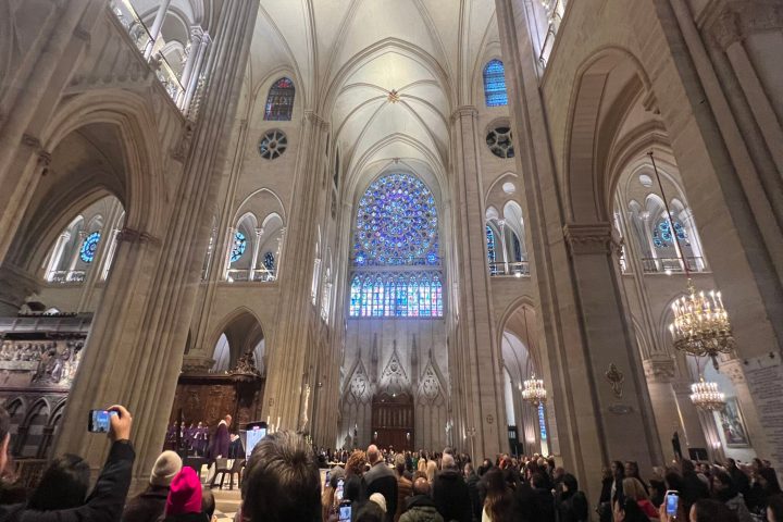 People inside a cathedral with vaulted ceilings and stained glass window.