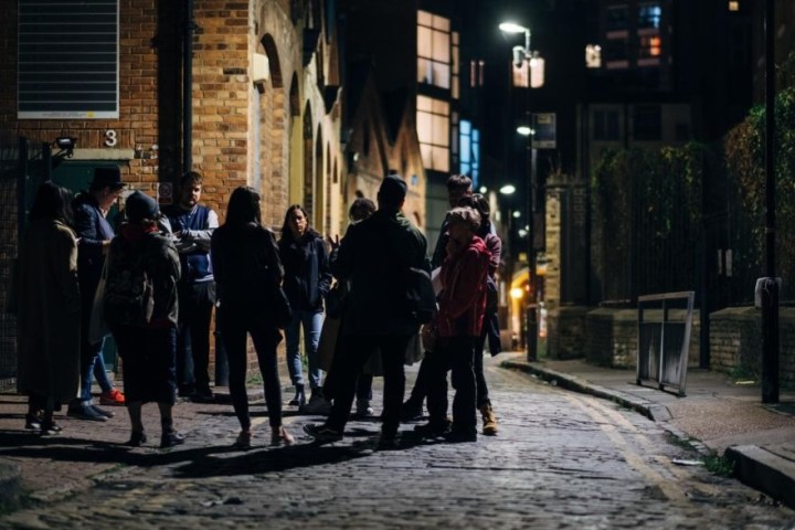 A group of people standing on a cobblestone street at night under streetlights.