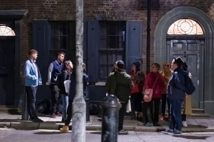 Group of people standing on a dimly lit street near a brick building at night.