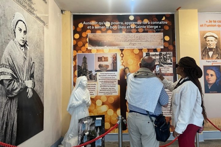 Two people view a religious exhibit with historical images and a statue.