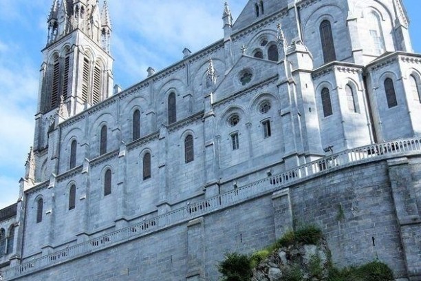 A tall, ornate stone cathedral with arched windows and a clock tower against a blue sky.