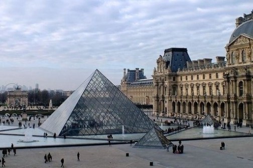 Glass pyramid and historic building at Louvre Museum with people walking nearby.